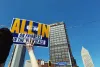 Arm holding up a flyer that says "All In on Fairness in the Workplace" with the buildings in the background of blue skies